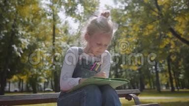 合上小美丽的学校女孩用彩色铅笔画画，<strong>坐在</strong>阳光明媚的<strong>公园里</strong>的长凳上。 慢动作镜头。
